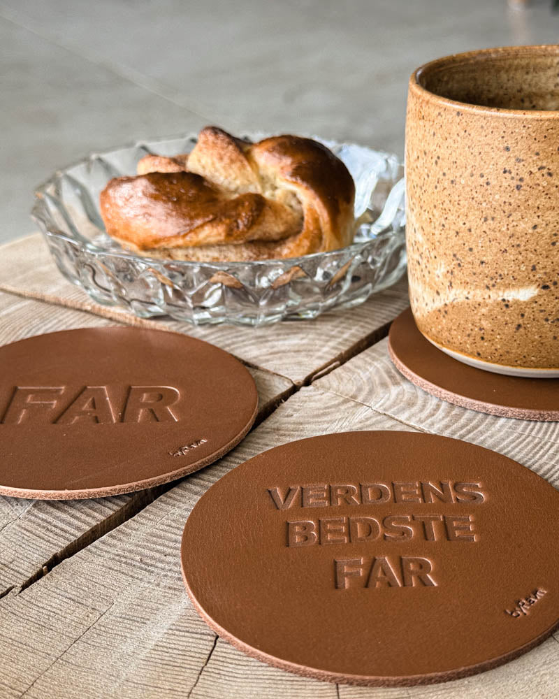MOKKA glassbrikker i cognac skinn preget "Far" og "Verdens bedste far" ved kaffekopp og kanelsnurr på trebord