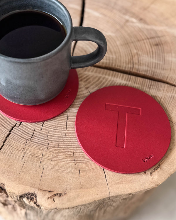 MOKKA glassbrikke i rødt skinn preget med bokstaven "T" på treskive ved grå kaffekopp på glassbrikke