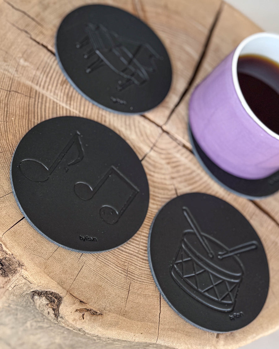 MOKKA glassbrikker i svart skinn preget med noter, tromme og flygel på treskive med lilla kaffekopp