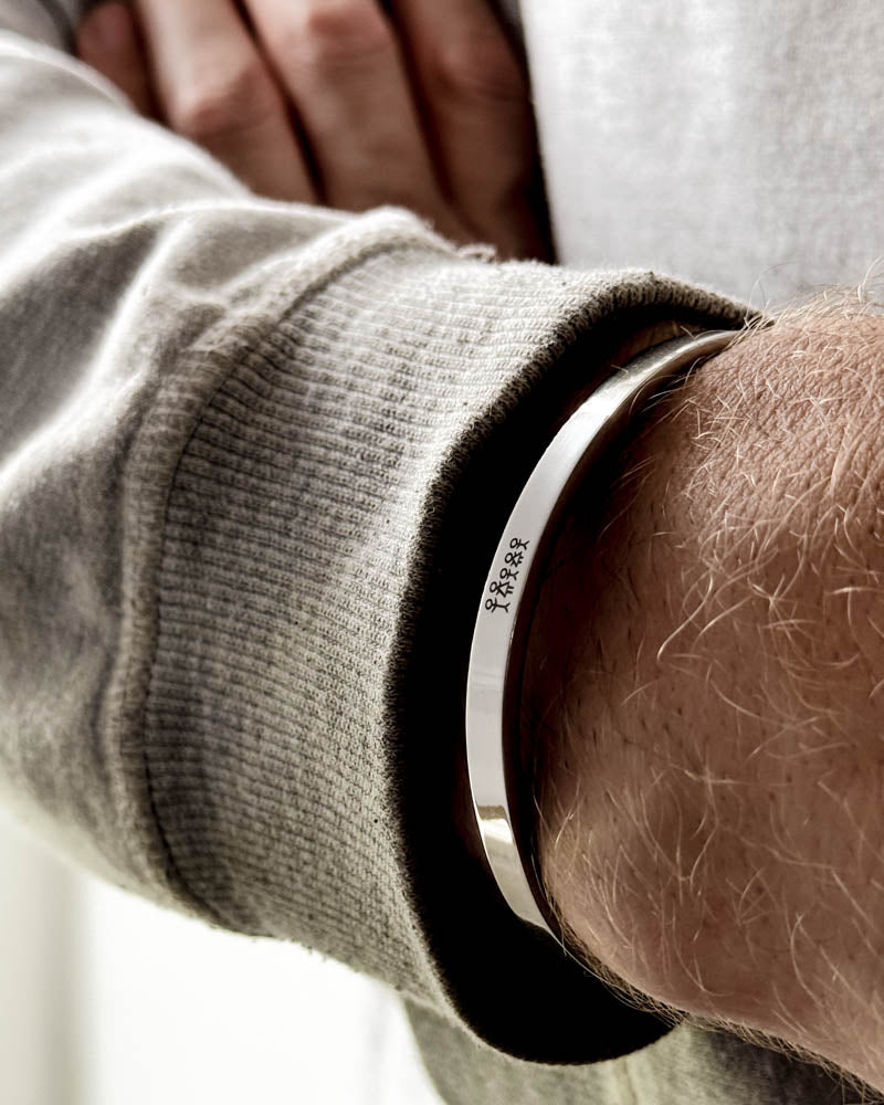 MARS STICK armbånd i sølvfarget rustfritt stål med gravert fyrstikkfamilie rundt et mannshåndledd, lysegrå sweatshirt