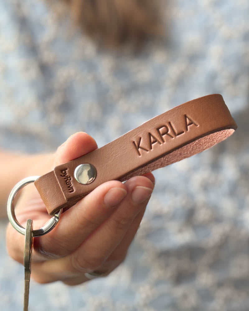RAVN nøkkelring i cognac skinn med navnet "Karla" gravert, holdt i hånden