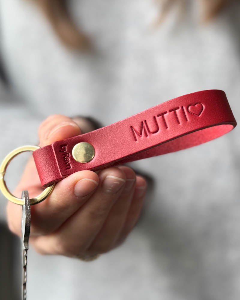 RAVN nøkkelring i rødt skinn med personlig gravering "Mutti" ♡ og messingnagle, holdt i hånden med nøkkel