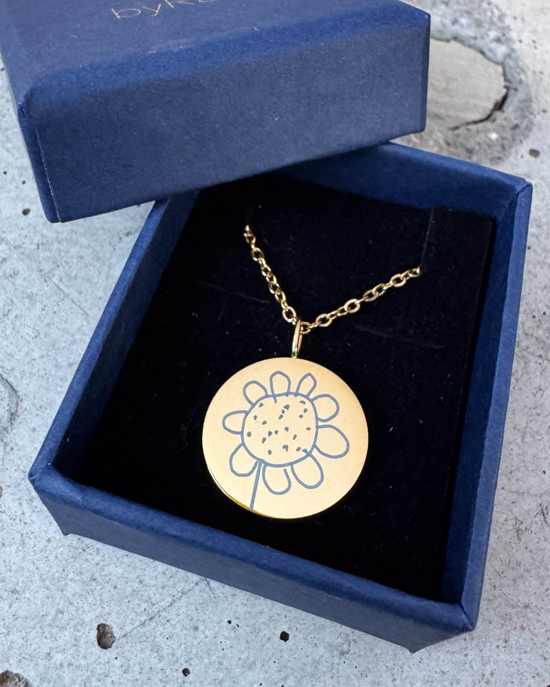 SIA MOTIF halskjede i gullbelagt stål med en barnetegning av en blomst gravert, i mørkeblå byRavn gaveeske