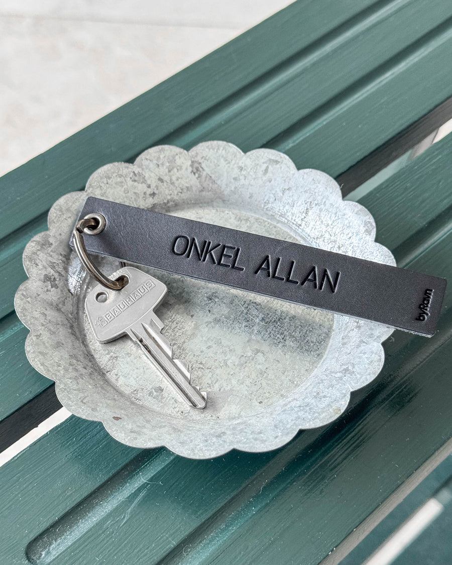 SOLO Large nøkkelring i svart skinn med graveringen "Onkel Allan" og nøkkel i sinkskål på grønn benk