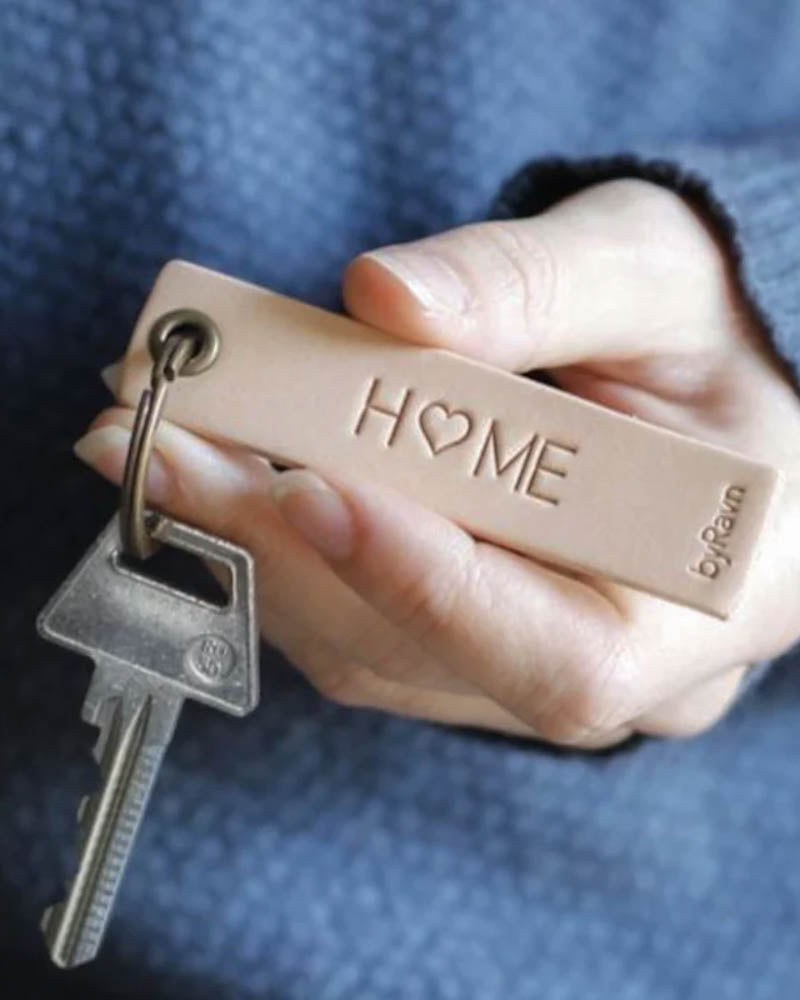 SOLO Small nøkkelring i naturfarget skinn holdt i hånden med nøkkel og graveringen "Home" med hjerte som O