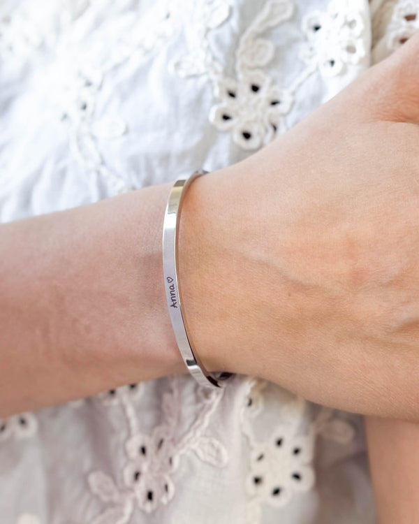 VENUS SCRIPT armbånd i sølvfarget rustfritt stål med navnet "Anna" ♡ i håndskrift rundt håndleddet, hvit brodert bluse