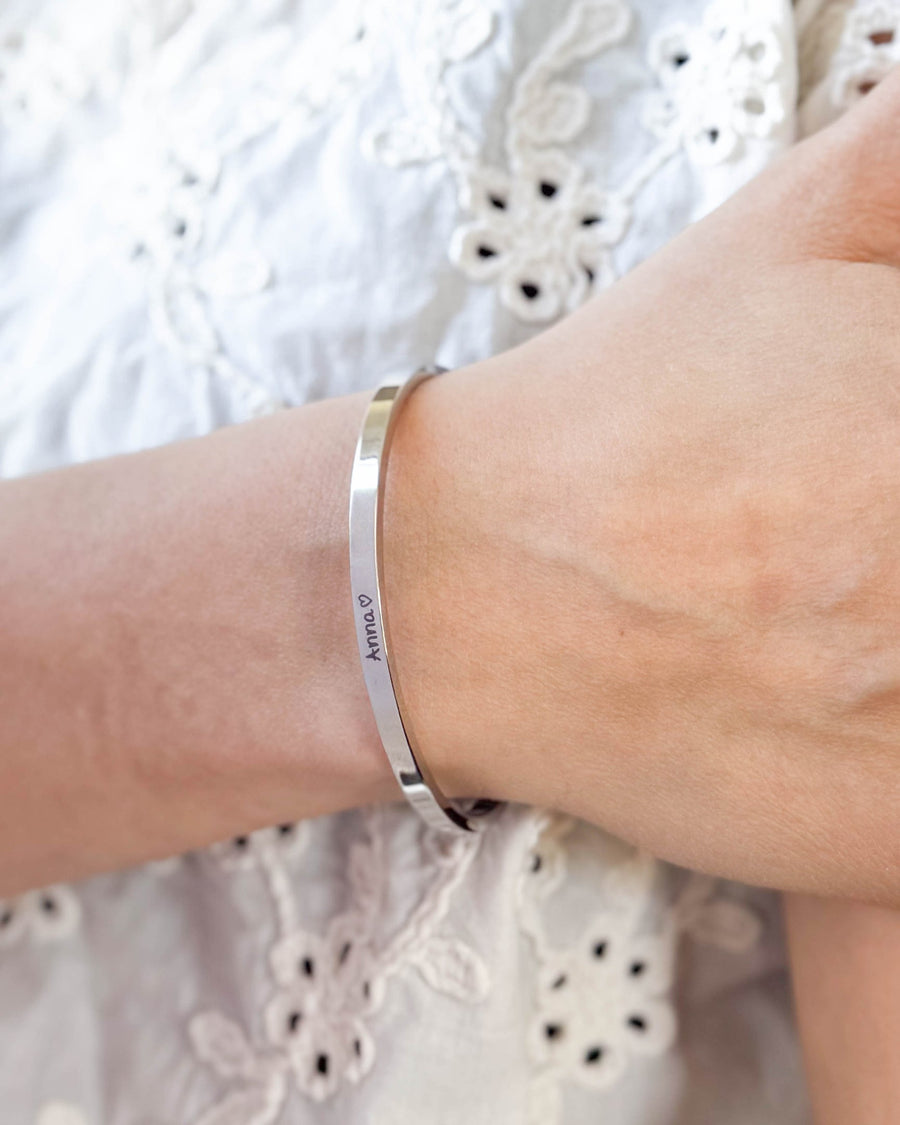 VENUS SCRIPT armbånd i sølvfarget rustfritt stål med navnet "Anna" ♡ i håndskrift rundt håndleddet, hvit brodert bluse