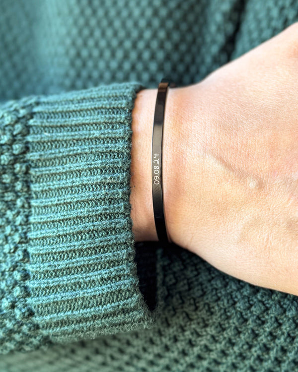 VENUS SCRIPT armbånd i svart stål med datoen "09.08.24" i håndskrift rundt håndleddet, grønn strikk