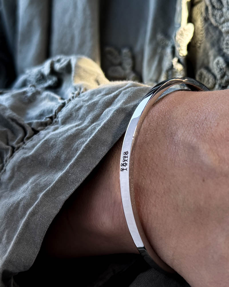 VENUS STICK armbånd i sølvfarget rustfritt stål med gravert fyrstikkfamilie, båret til grå bluse med puffermer