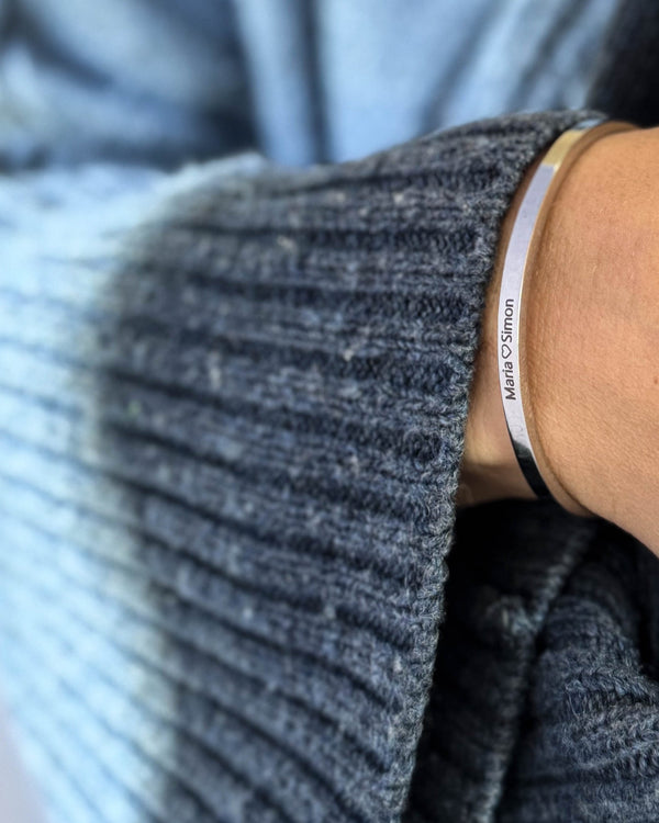 VENUS armbånd i sølvfarget rustfritt stål med graveringen "Maria ♡ Simon" rundt håndleddet, blå strikk