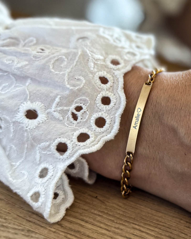 ZOE navnearmbånd i gullbelagt stål med navnet "Amalie" ♡ gravert, båret rundt håndleddet til hvit blondebluse